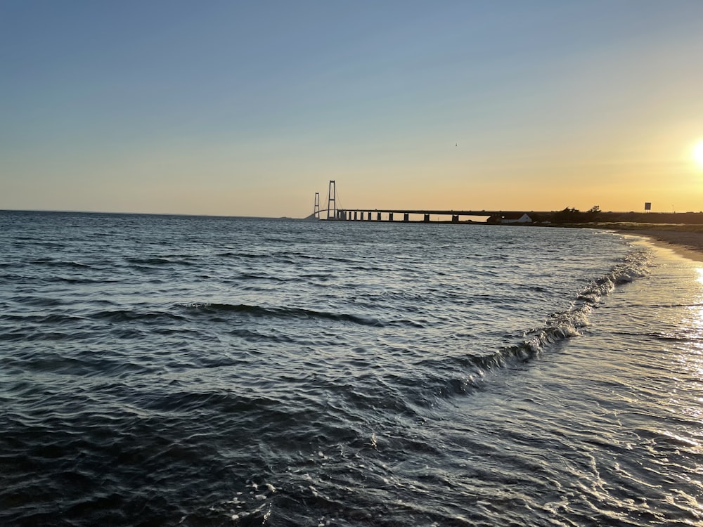 the sun is setting over the ocean with a bridge in the distance