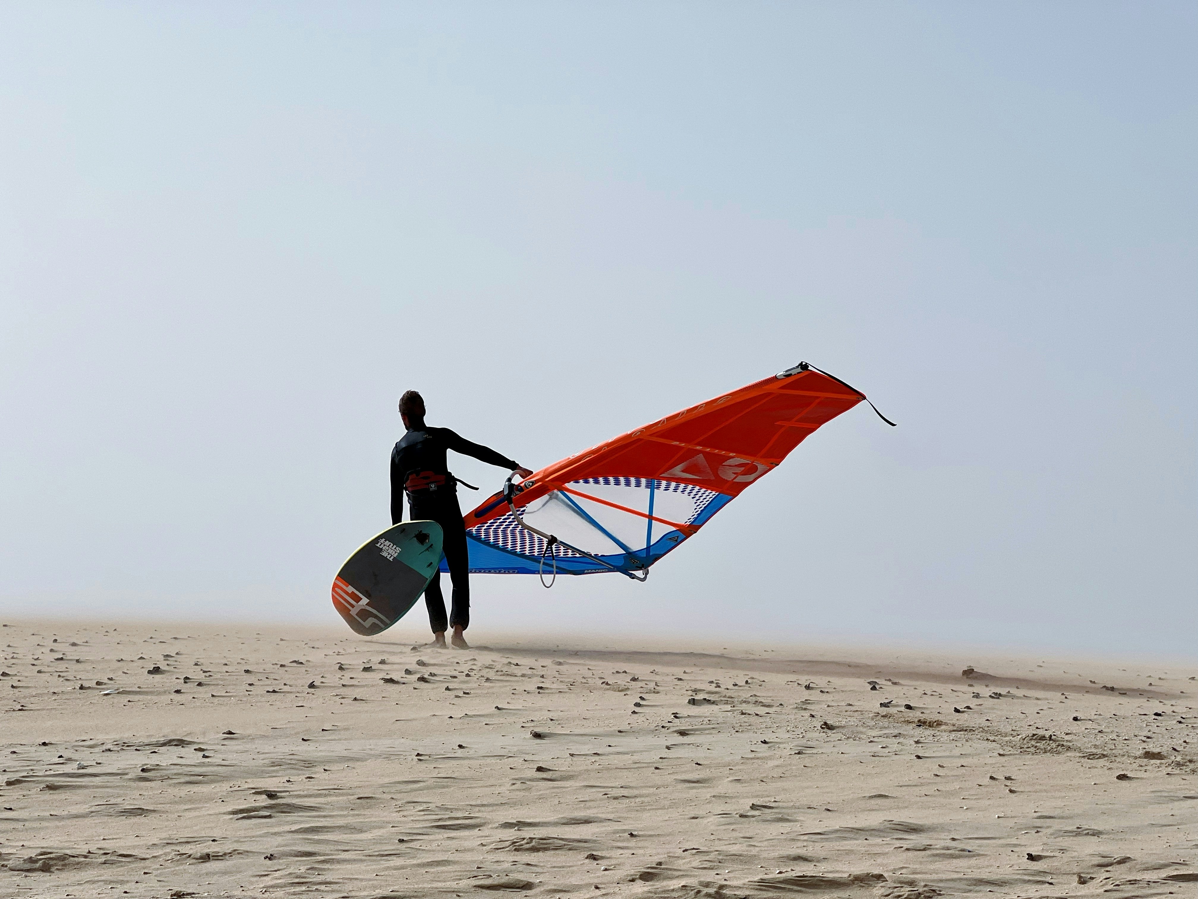 a man holding a surfboard and a kite on a beach