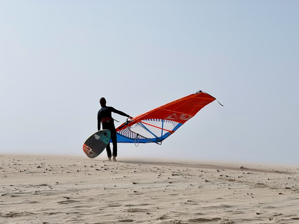 a man holding a surfboard and a kite on a beach