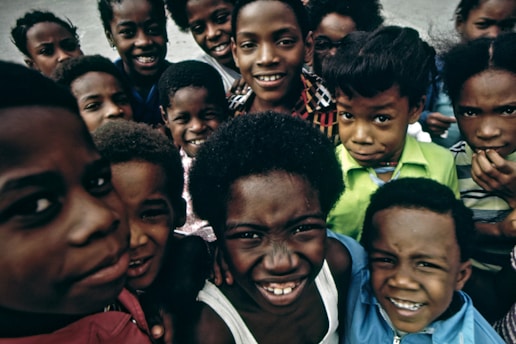 A group of smiling children huddled closely together, expressing joy and playfulness. Their bright expressions and lively eyes convey a sense of camaraderie.