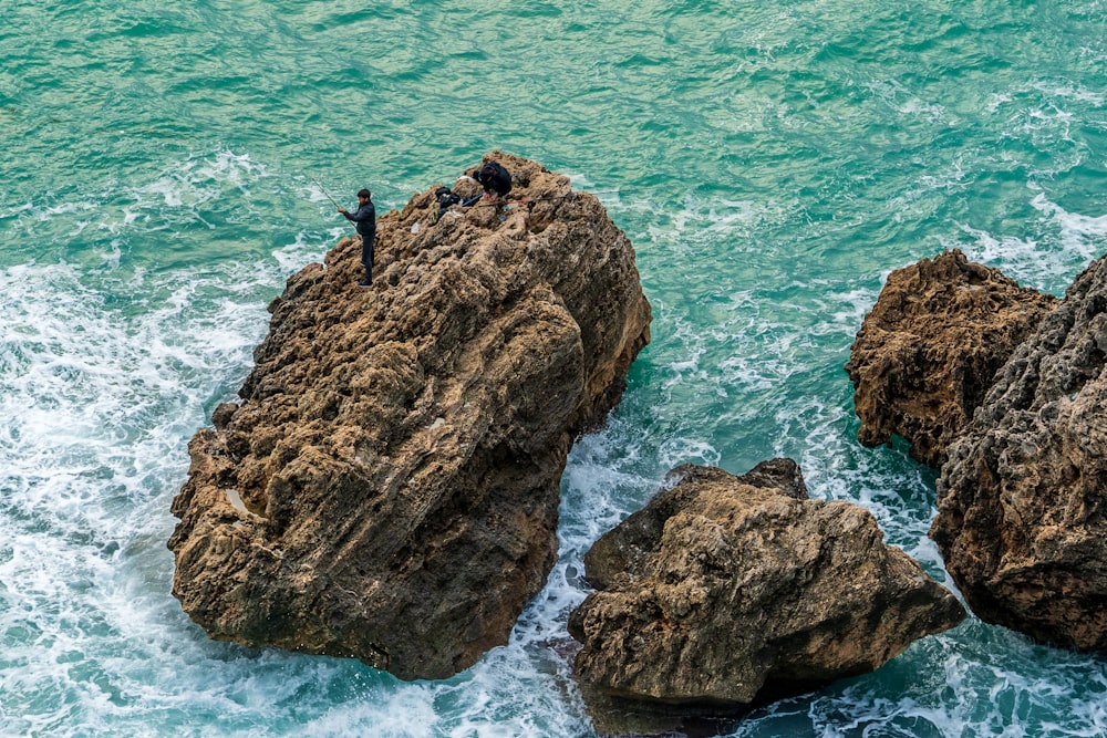 a group of people standing on top of a large rock next to the ocean