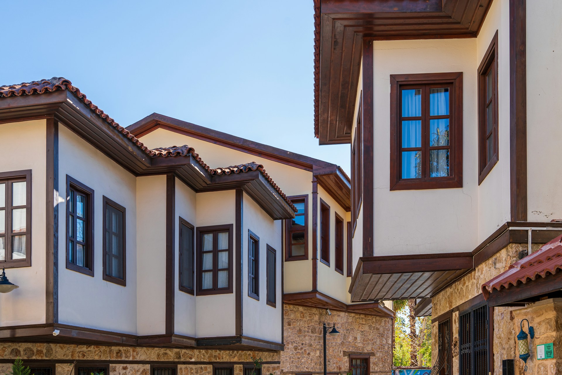 Traditional architecture with wooden-framed windows and stone walls. The buildings have tiled roofs and a warm exterior palette, set against a clear blue sky.