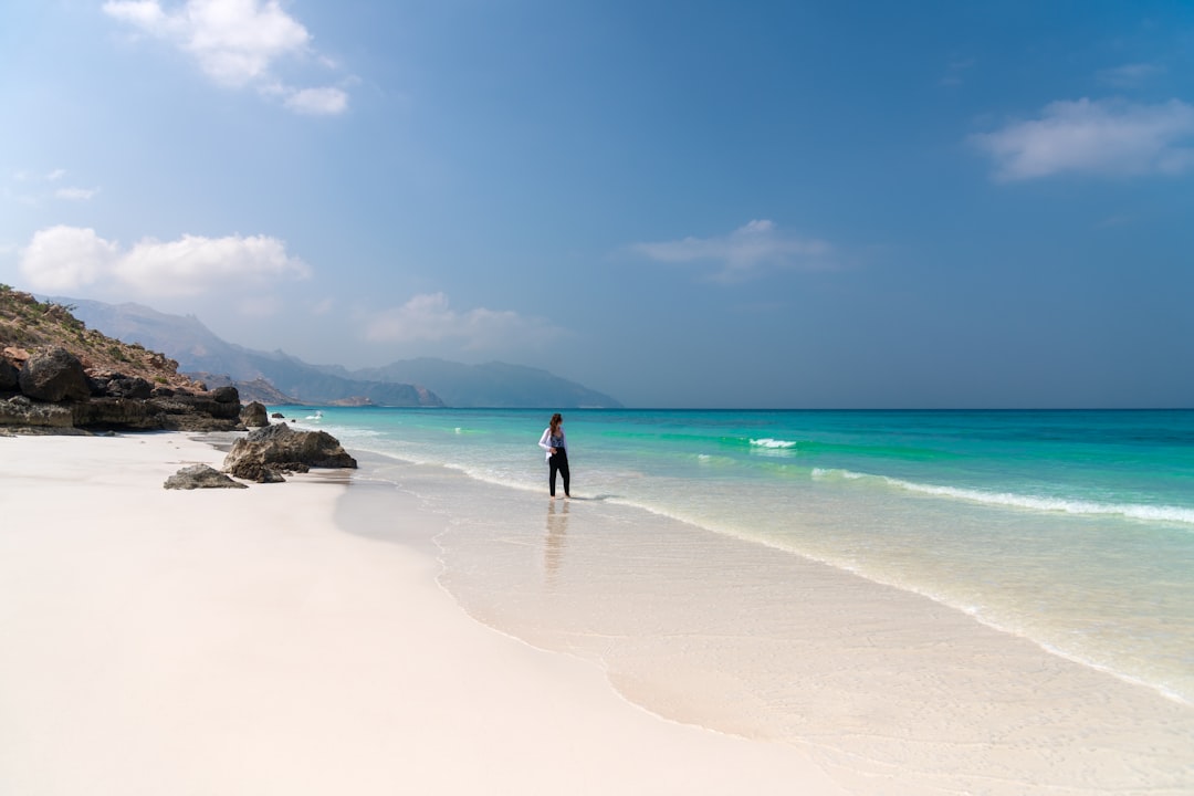 a man standing on a beach holding a surfboard, Beautiful pristine white sand beaches on the Socotra island. Here you can