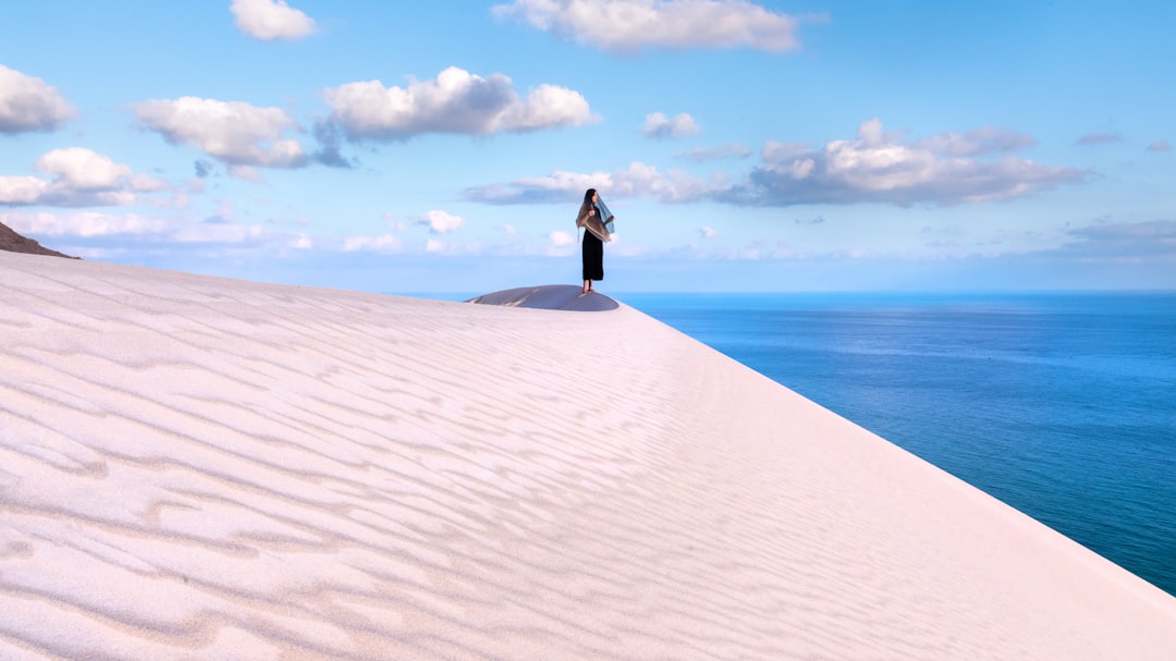 a person standing on top of a sand dune, Girl meets sunrise on a huge dune above the ocean on the Socotra island