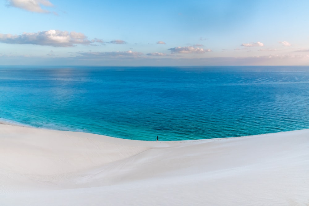 a person standing on top of a sandy hill next to the ocean