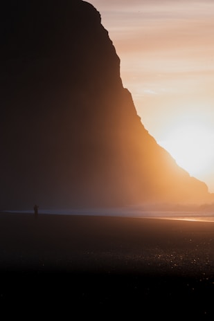 A dramatic sunset scene captured on film, highlighting a silhouette of a lone figure on a cliff.