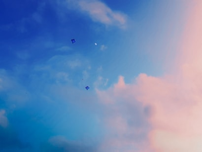 A serene sky with a gradient of blue and pink colors, featuring a few kites flying against scattered clouds. The scene conveys a sense of calm and openness.