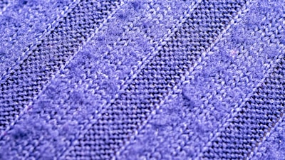 A close-up view of a textured fabric with a zigzag knit pattern. The material appears soft and has alternating light and dark blue stripes.