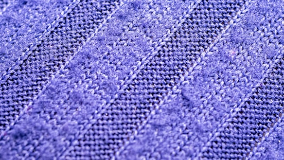 A close-up view of a textured fabric with a zigzag knit pattern. The material appears soft and has alternating light and dark blue stripes.