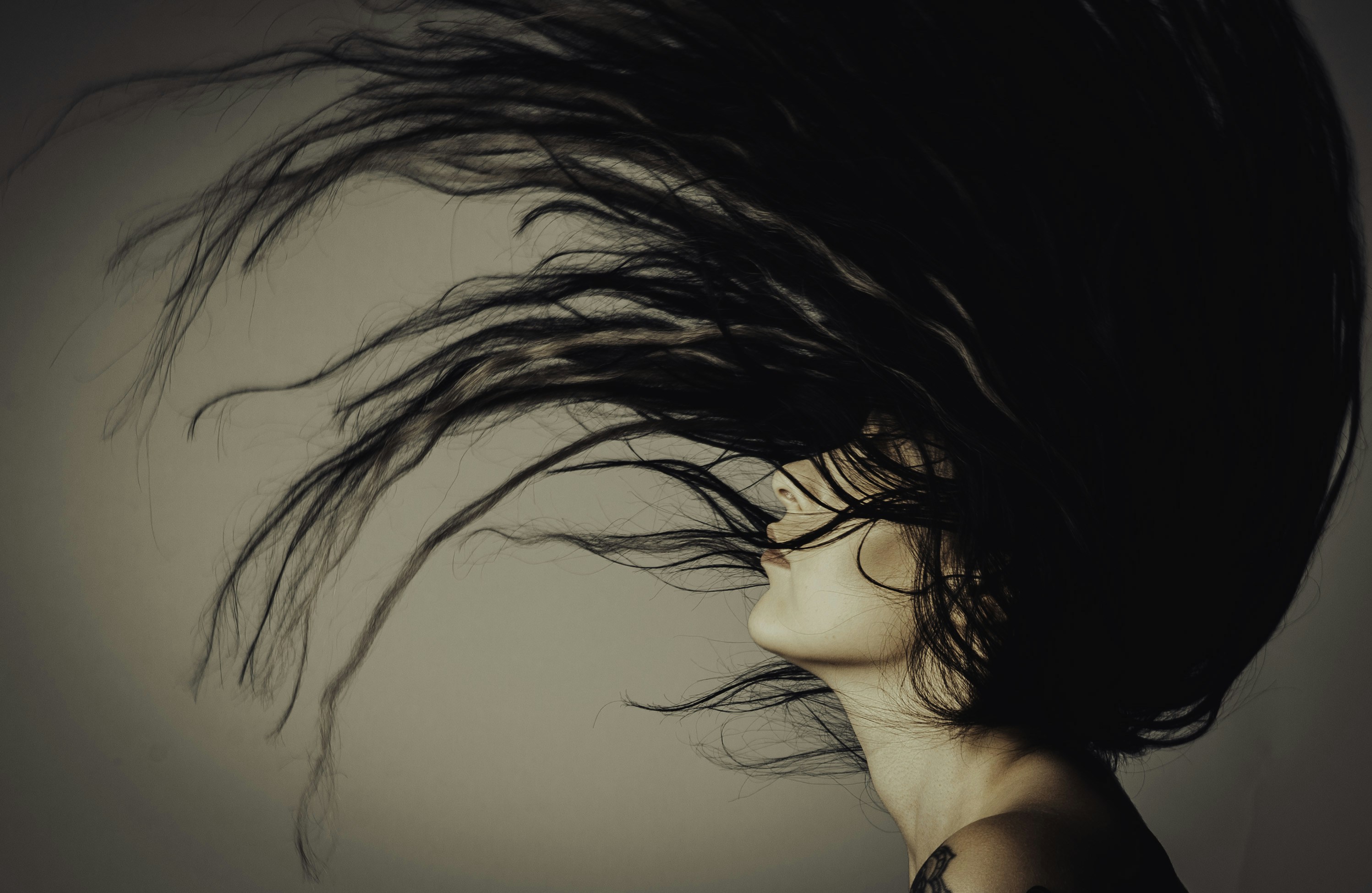 A woman throwing back her head with her long black hair flying above her head.