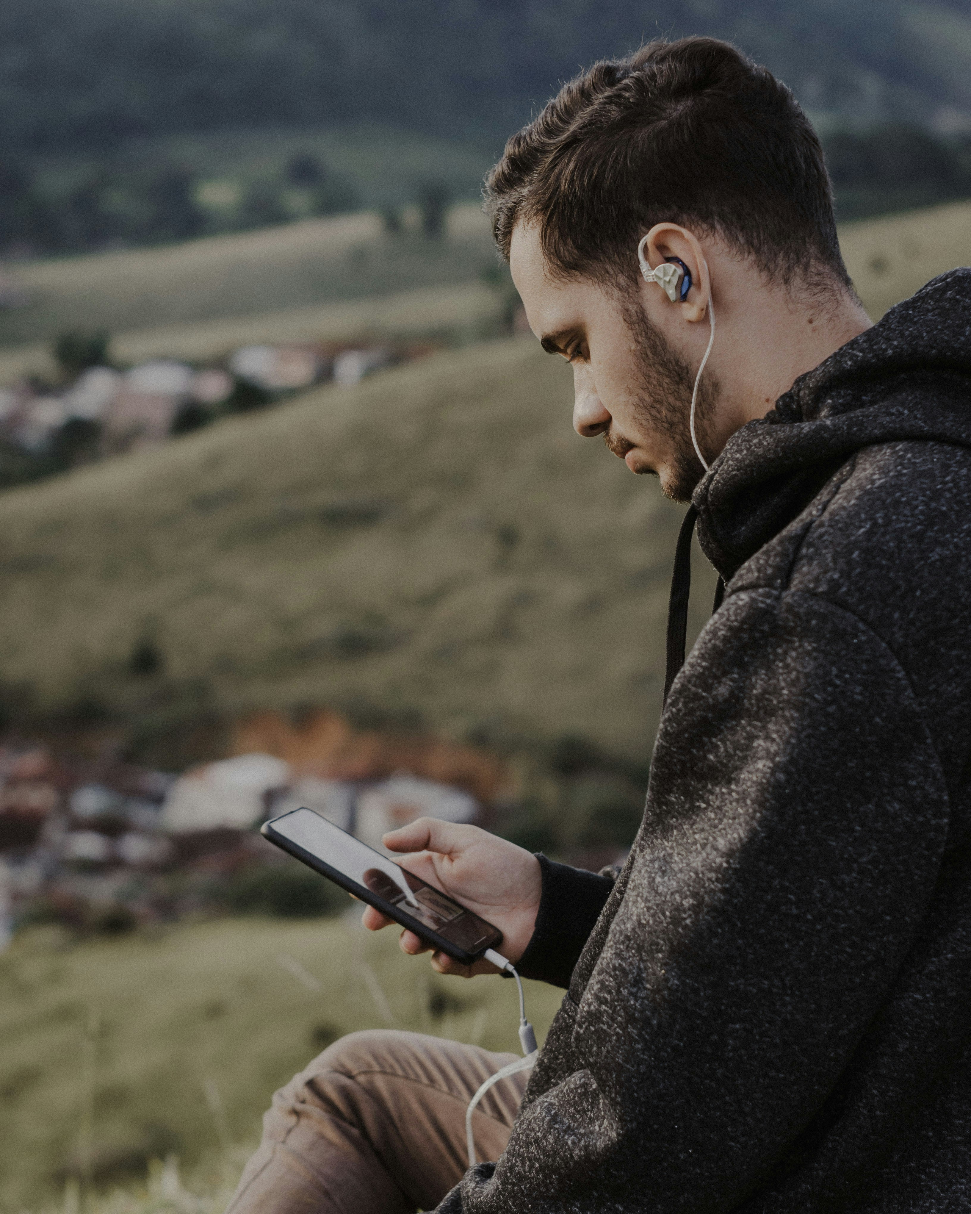 a man sitting on a hill looking at his phone