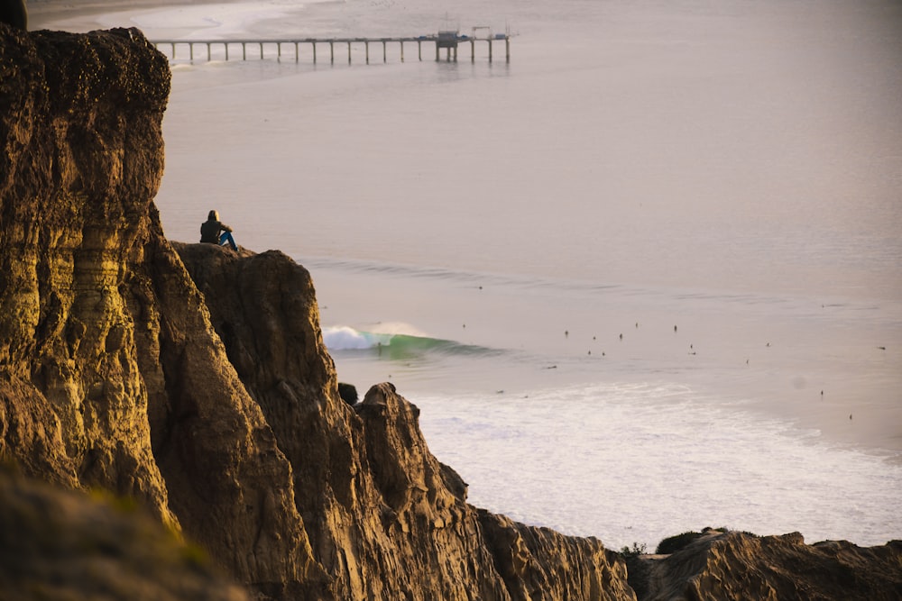 a person sitting on top of a cliff next to the ocean