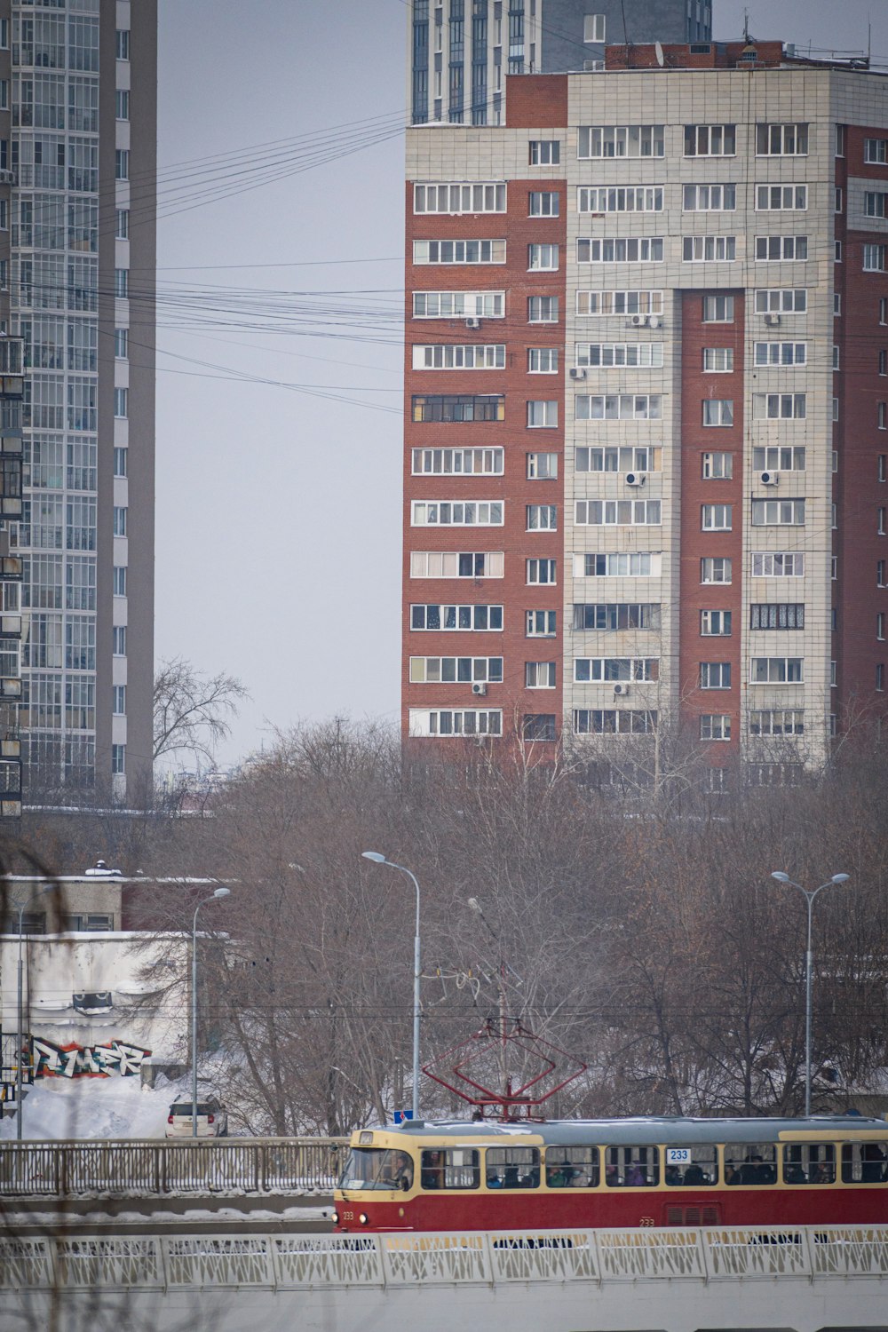 a red and yellow train traveling past tall buildings