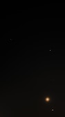 A dark night sky scattered with a few bright celestial bodies, including distant stars and what appears to be a planet or moon with a glowing aura. The prominence of the celestial object at the bottom right creates a sense of depth and distance.
