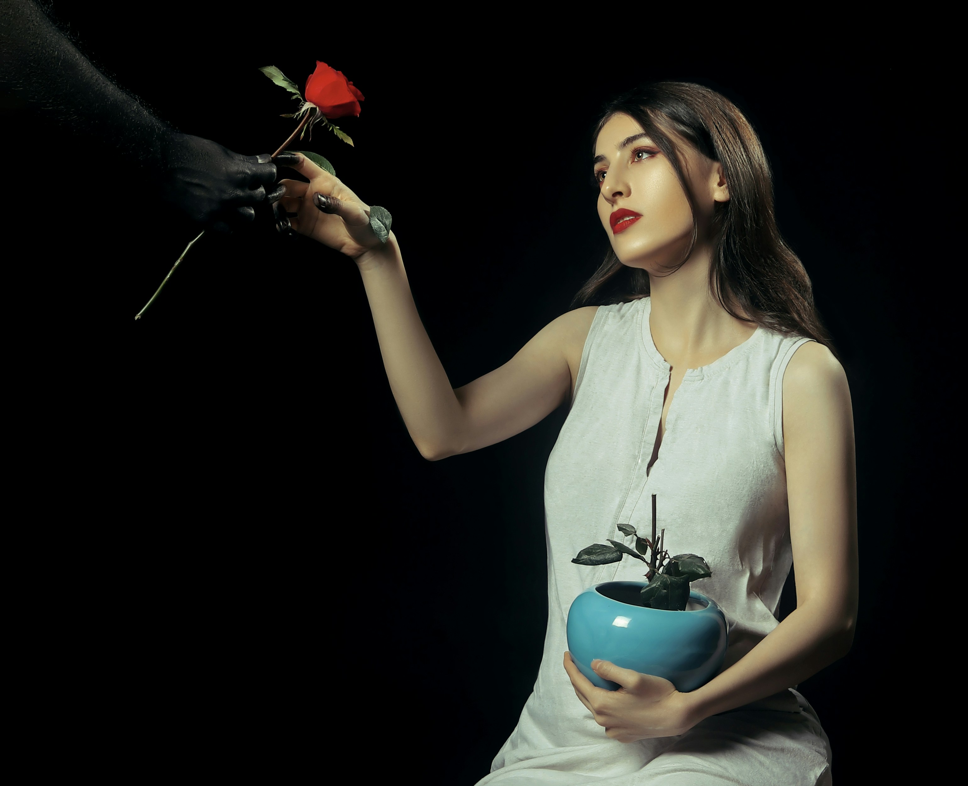 a woman in a white dress holding a blue vase with a red rose in it