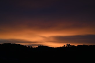 the sun is setting over the mountains and trees