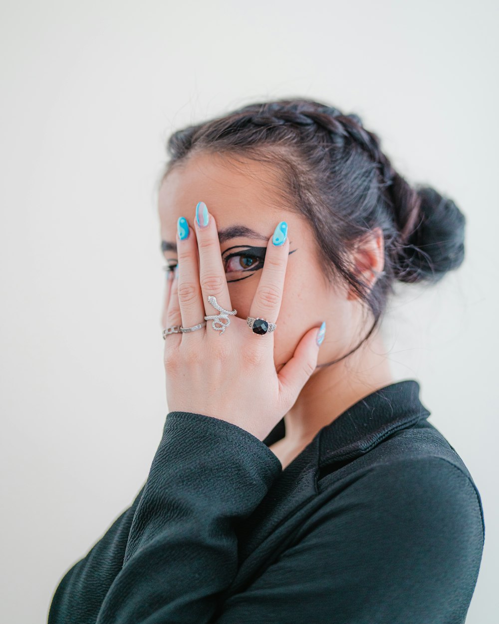 a woman with blue and black nail polish holding her hands to her face