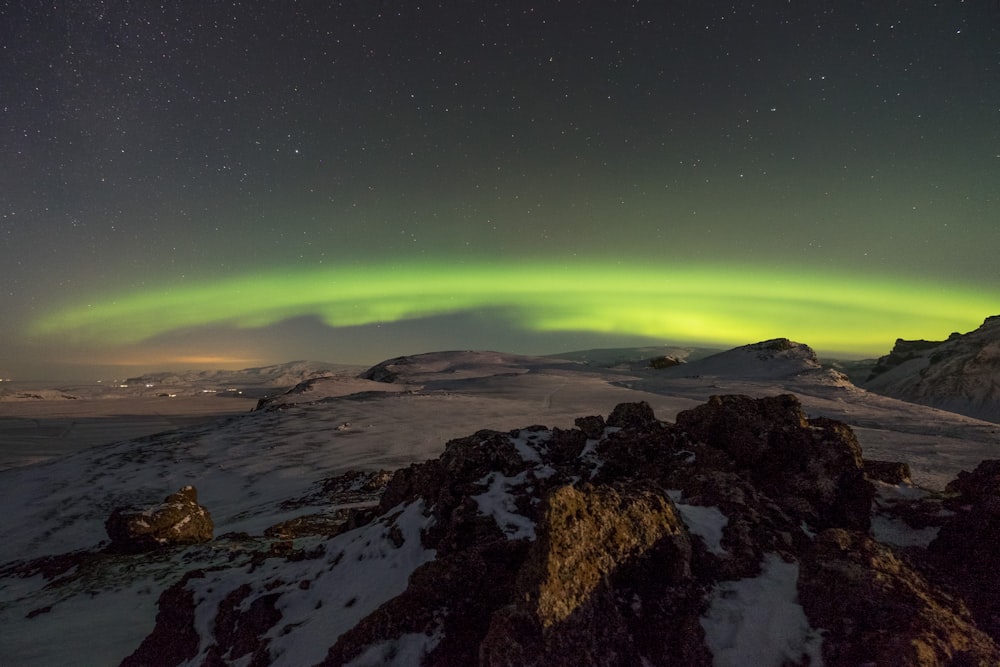a green and yellow aurora above a snowy mountain