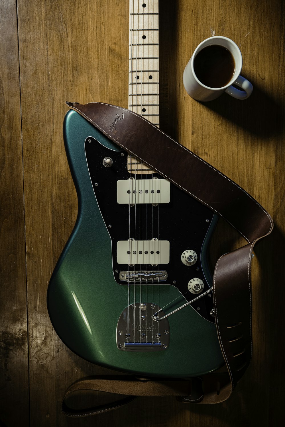 uma guitarra verde sentada em cima de uma mesa ao lado de uma xícara de café