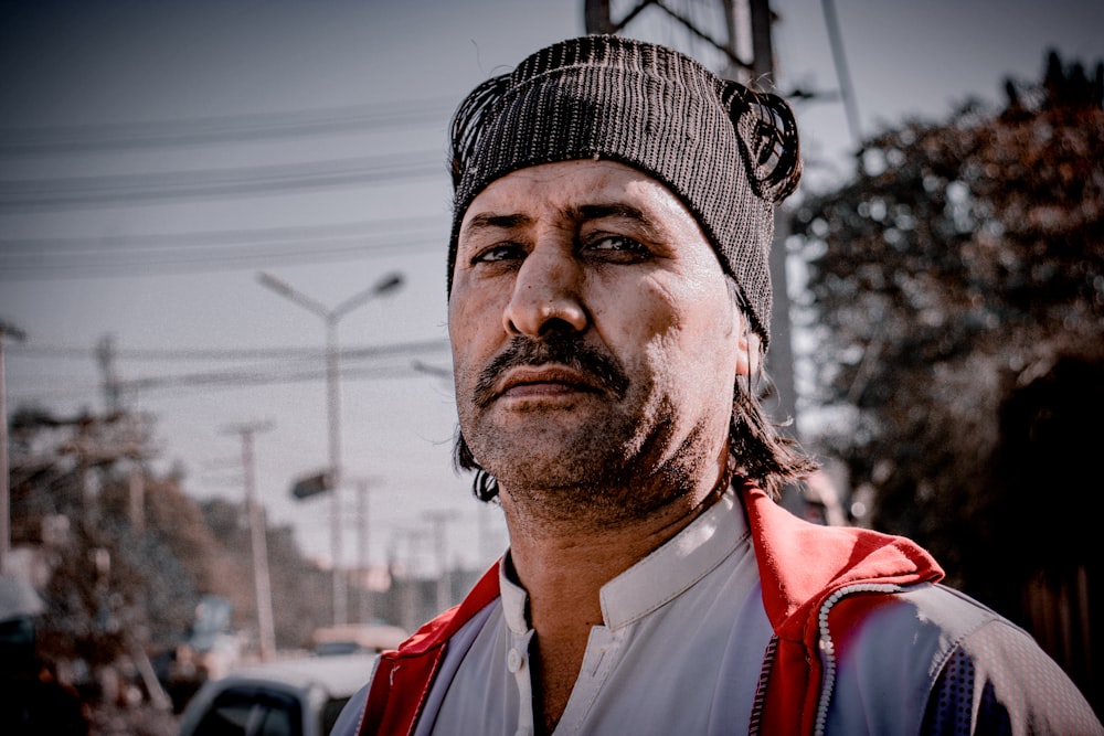 a man wearing a hat and vest standing in front of a street