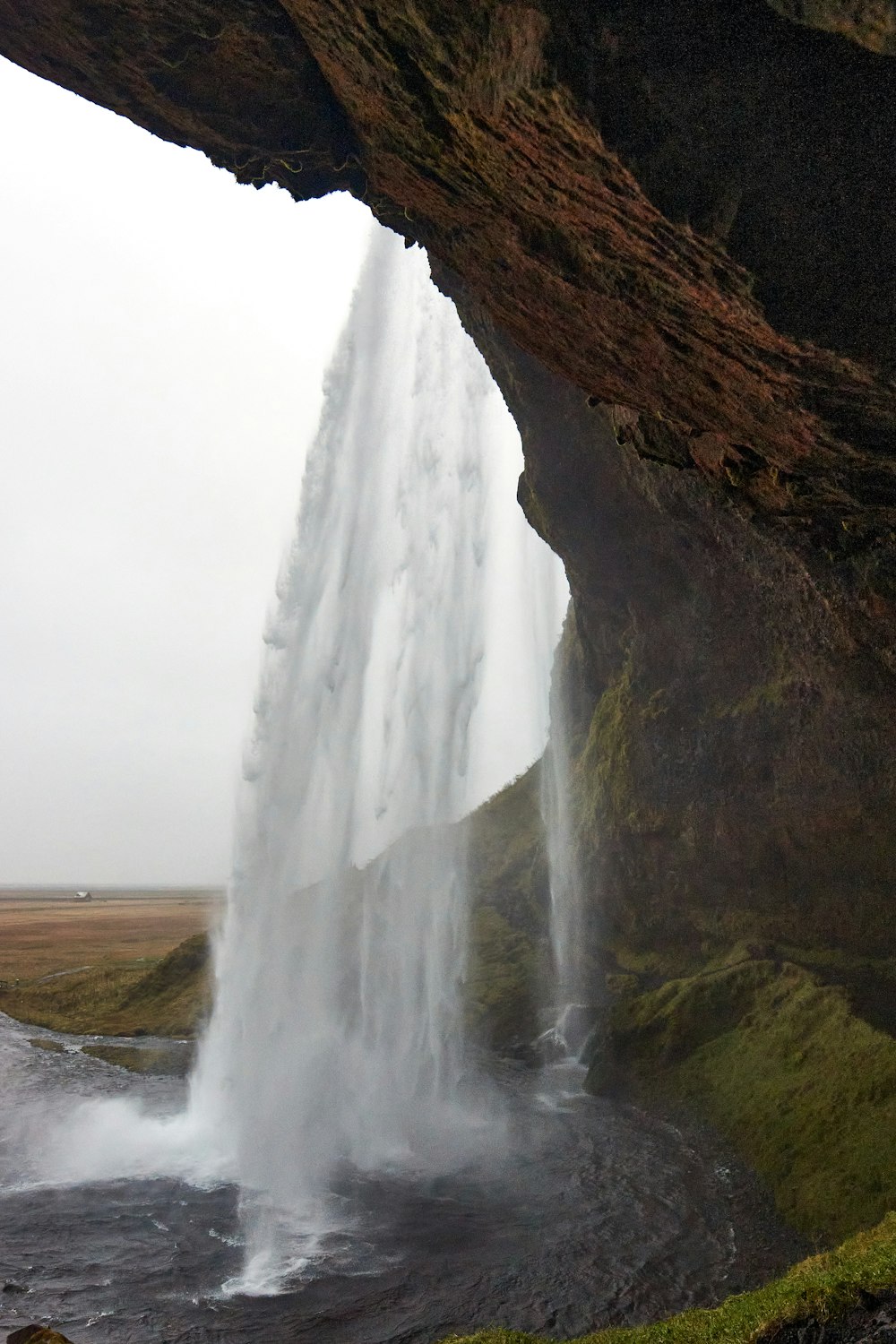 a large waterfall is seen through an opening in the side of a cliff