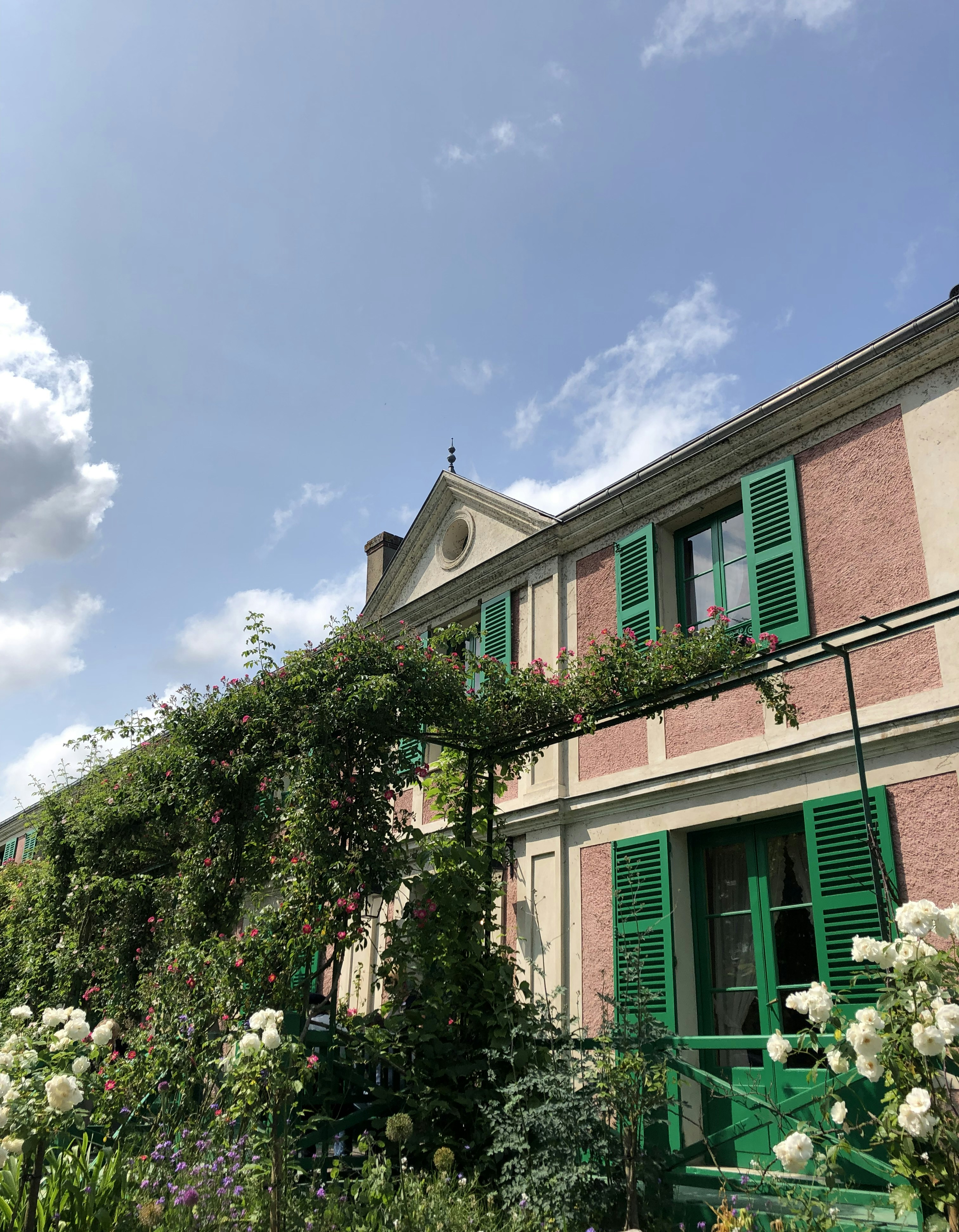 a building with green shutters and flowers in front of it