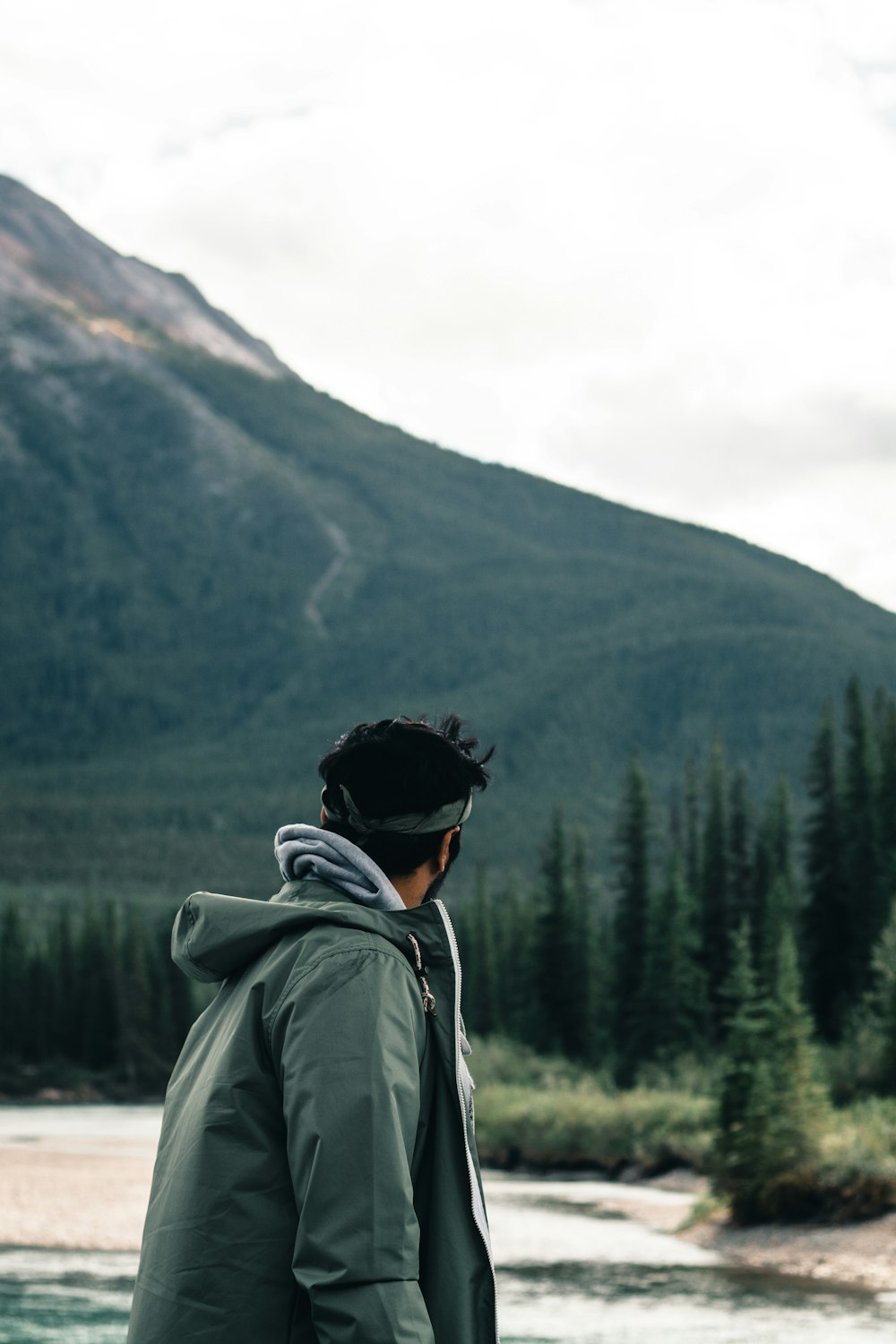 a man standing in front of a river with a mountain in the background