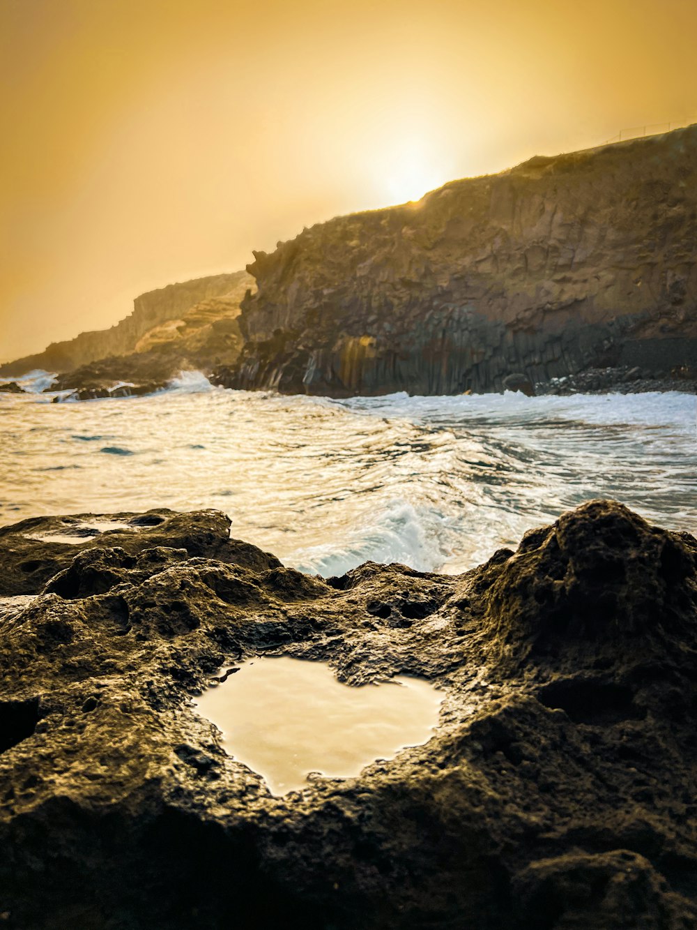 the sun is setting over the ocean and rocks