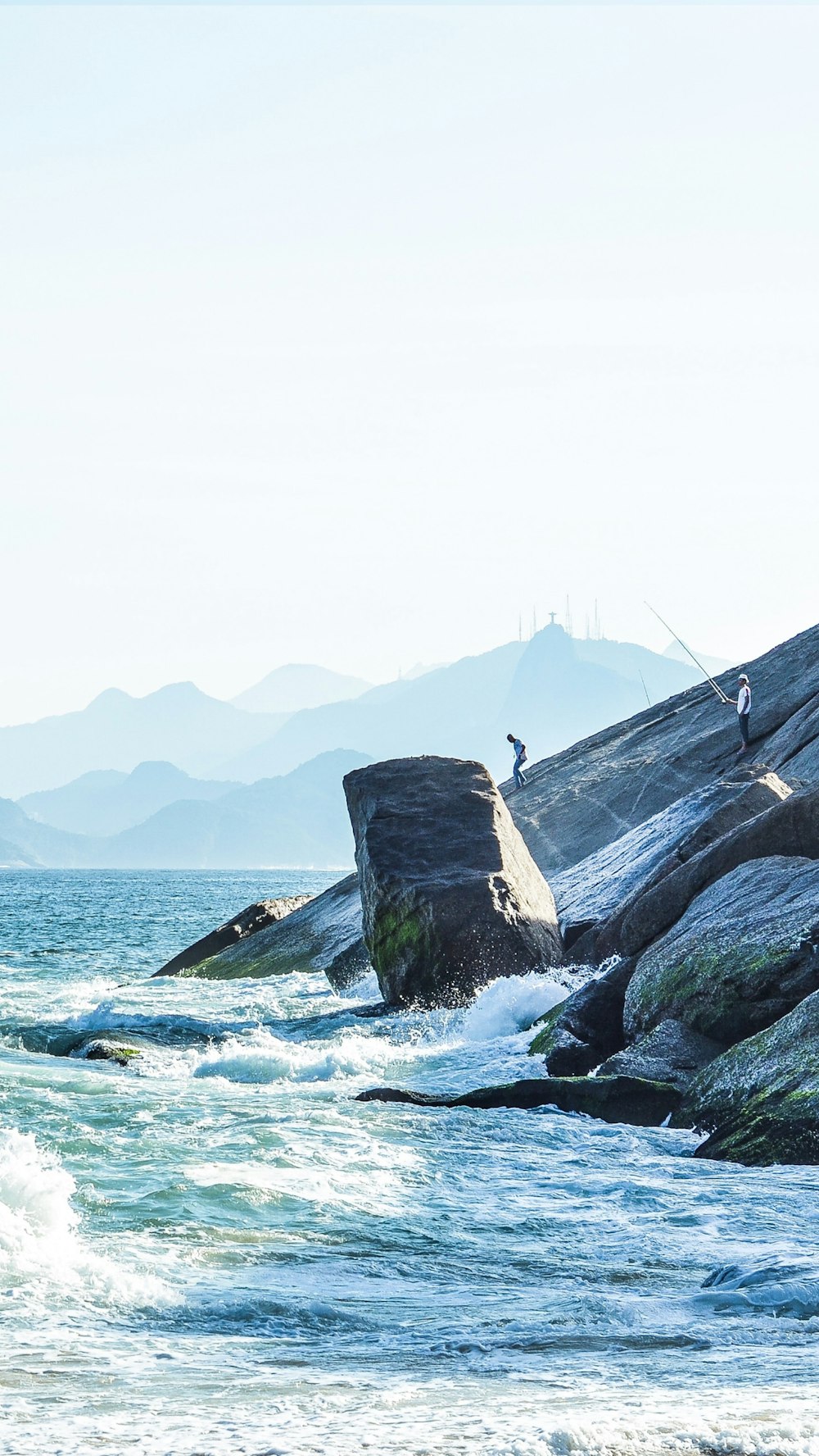 a man standing on top of a rock next to the ocean