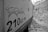 A close-up, black and white photograph focuses on the side panel of a construction vehicle with the text '210LC-7H' and a stylized logo. The background shows an indistinct, rocky terrain suggesting a construction or industrial site.