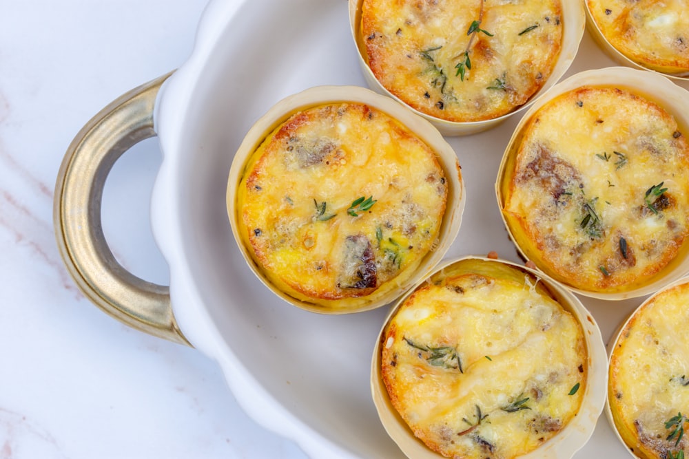 um prato branco coberto com mini quiches cobertas de queijo