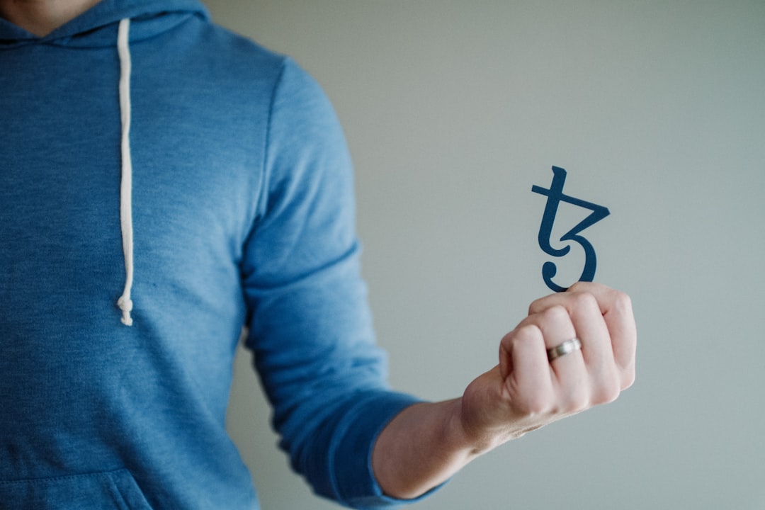 a man in a blue hoodie is holding a piece of paper, Man holding tezos logo