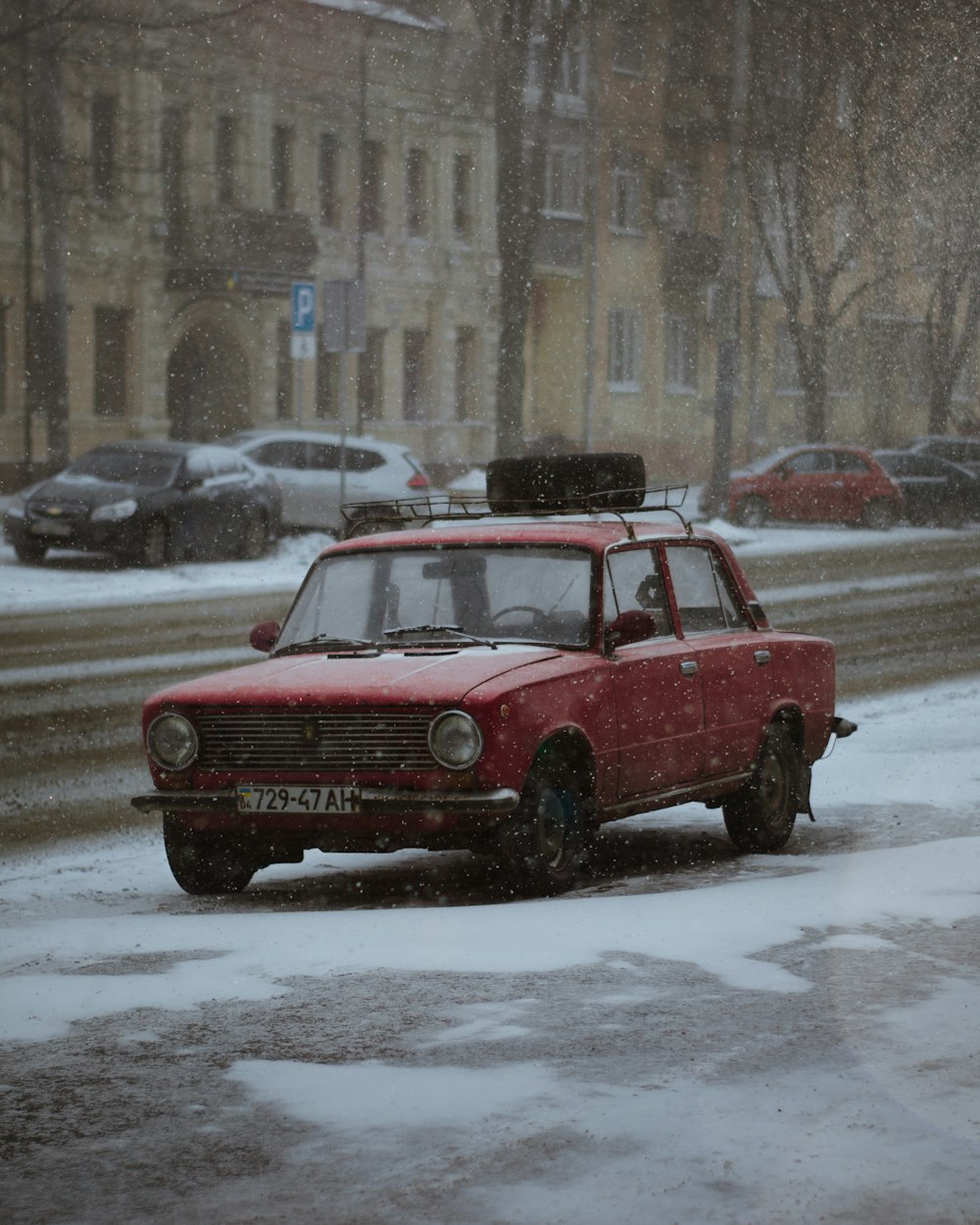 a red car driving down a snow covered street