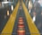 A shiny floor surface features two parallel yellow lines, with reflections of colorful lights scattered across it. In the center between the yellow lines, a gridded pattern runs along the ground, illuminated with orange and red hues.