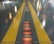 A shiny floor surface features two parallel yellow lines, with reflections of colorful lights scattered across it. In the center between the yellow lines, a gridded pattern runs along the ground, illuminated with orange and red hues.