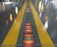 A shiny floor surface features two parallel yellow lines, with reflections of colorful lights scattered across it. In the center between the yellow lines, a gridded pattern runs along the ground, illuminated with orange and red hues.