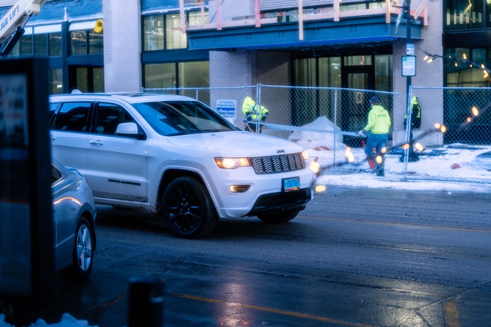 a white jeep driving down a street next to a tall building