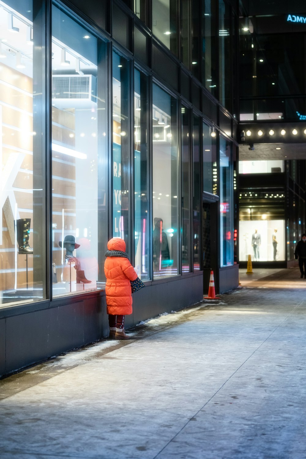 a little boy in a red jacket looking in a store window