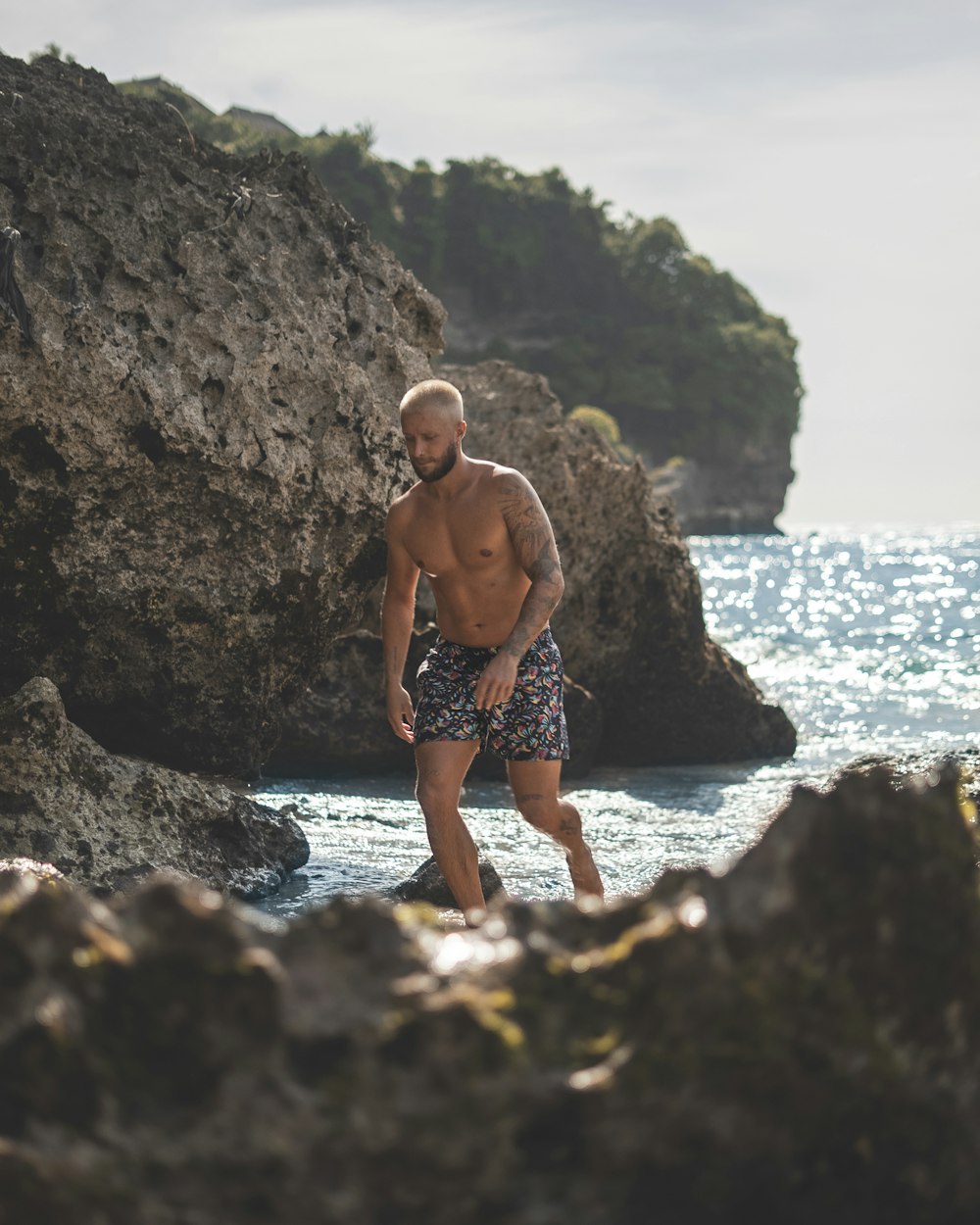 Un hombre sin camisa parado en una playa rocosa junto al océano