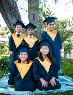 a group of children in graduation gowns sitting under a tree