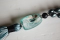 A close-up view of a decorative piece featuring a large, rectangular turquoise bead with a textured surface, paired with a tassel and dark, metallic beads strung together. The main bead has a rugged, weathered appearance with visible holes and a speckled pattern.