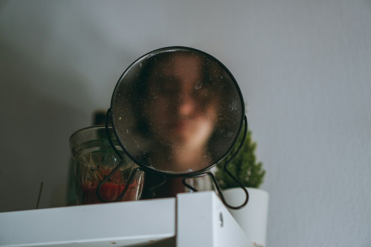 Volto sfocato riflesso in uno specchietto rotondo su una mensola, il riconoscersi vagamente in ogni etichetta