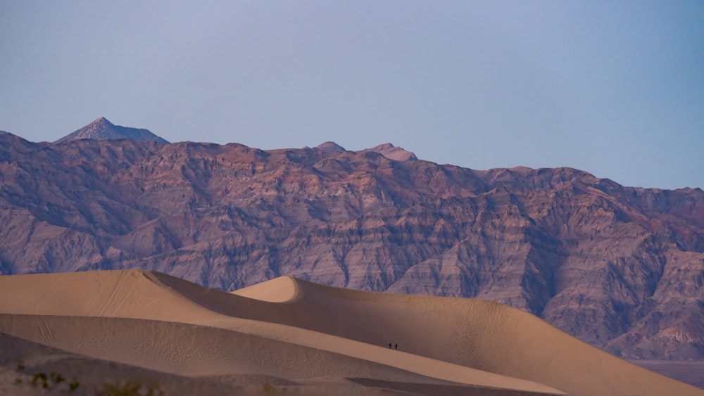 a mountain range in the distance with sand dunes in the foreground