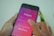 A person holding a smartphone displaying the Instagram login screen. The screen shows fields for entering a username and password, with options for password recovery and Facebook login. The background is blurred, revealing hints of green and white colors.