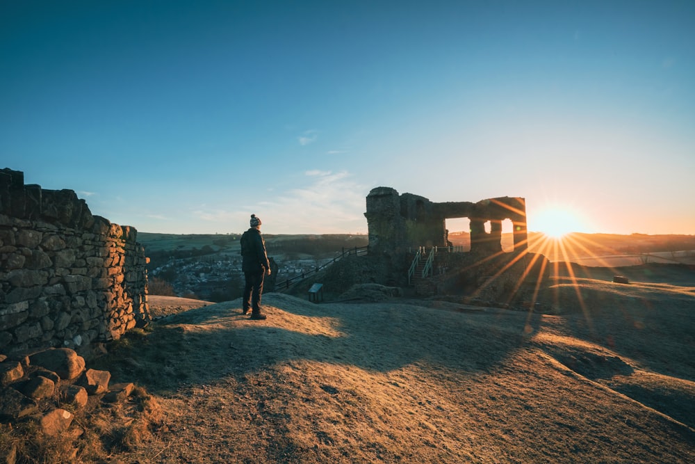 a man standing on top of a hill next to a stone wall