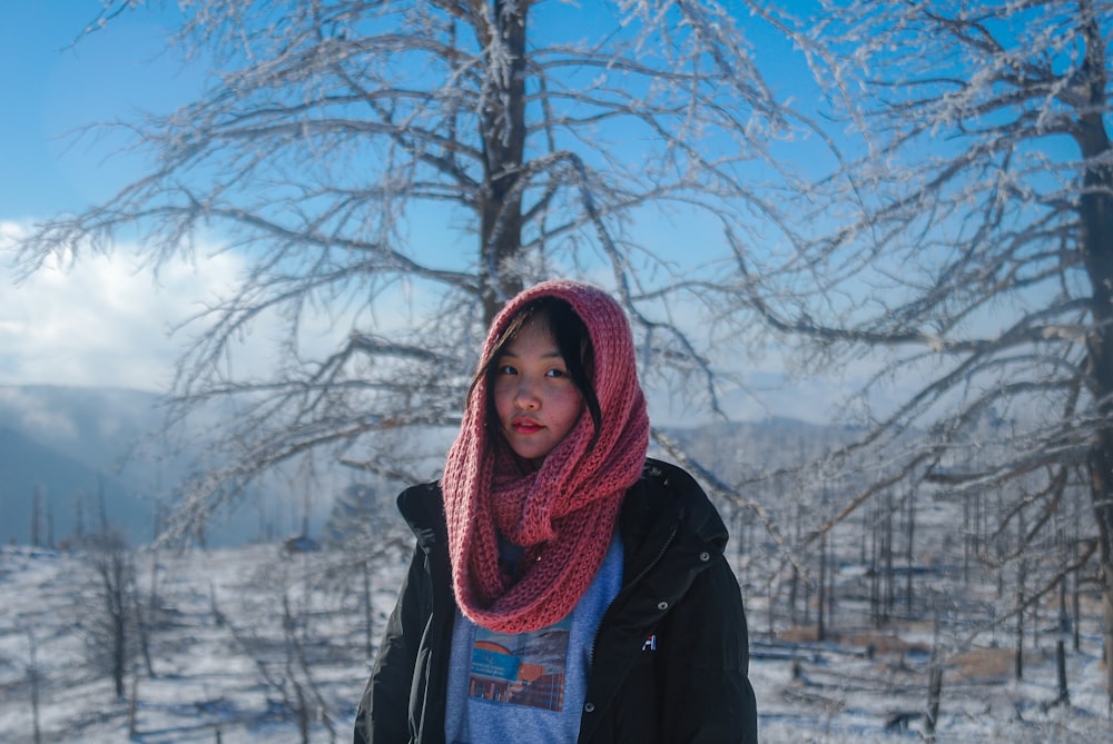 a woman standing in the snow in front of a tree