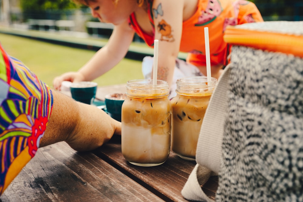 a woman sitting at a picnic table with two drinks in front of her