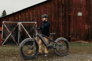 a man standing next to a bike in front of a barn