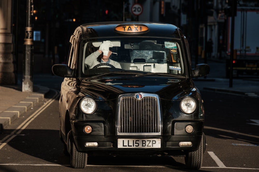 a black taxi cab driving down a street next to a tall building