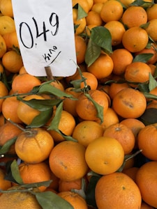 A pile of oranges with green leaves, accompanied by a price sign indicating 0.49 per kilo.